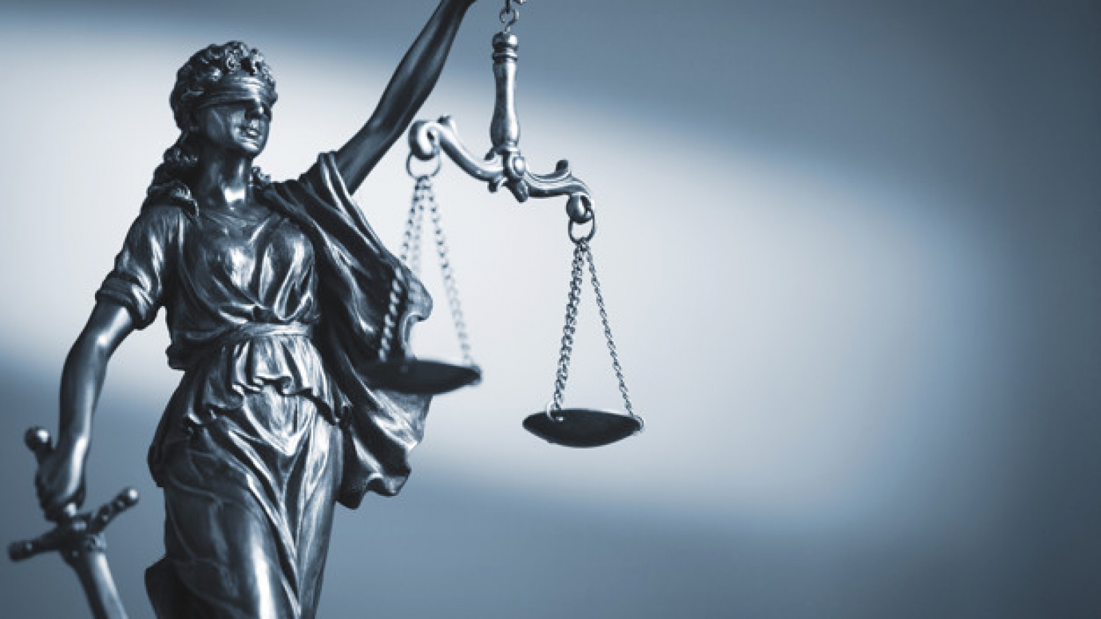 Blindfolded figure of Justice holding scales and a sword conceptual of the courts, judgement, law and order in a beam of light over a grey background with copy space